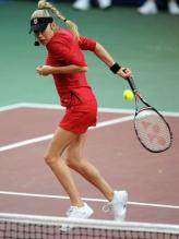 Anna Kournikova in a red tennis outfit hits a ball behind her back.JPG